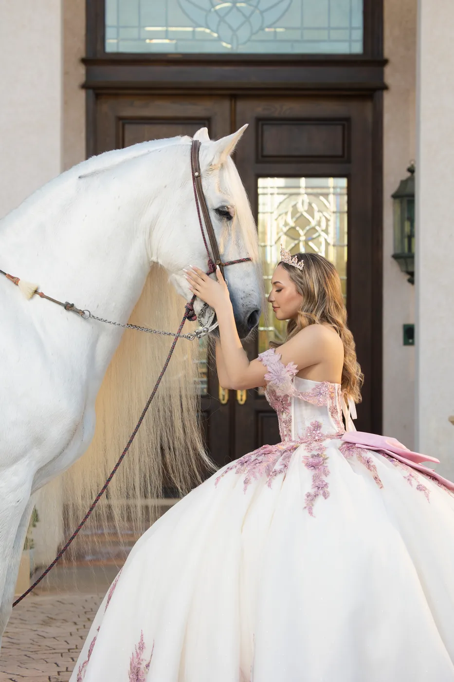 Quinceañera in a white and lilac gown greeting a white horse