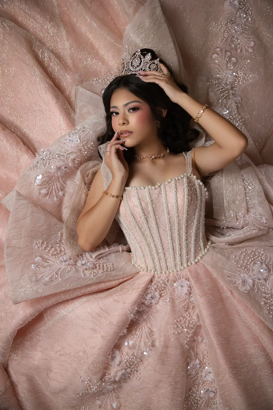 Quinceañera in a blush beaded gown and crown resting on her skirt