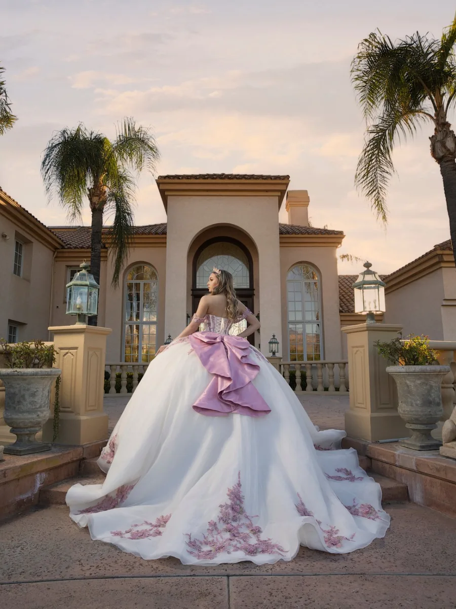 Quinceañera in a white gown with a pink bow on the steps of the Rancho Jalisco estate at sunset