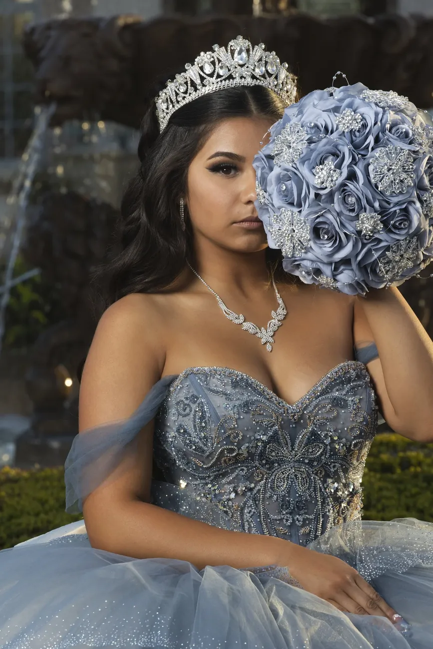 Quinceañera in a blue gown holding a bouquet of blue roses