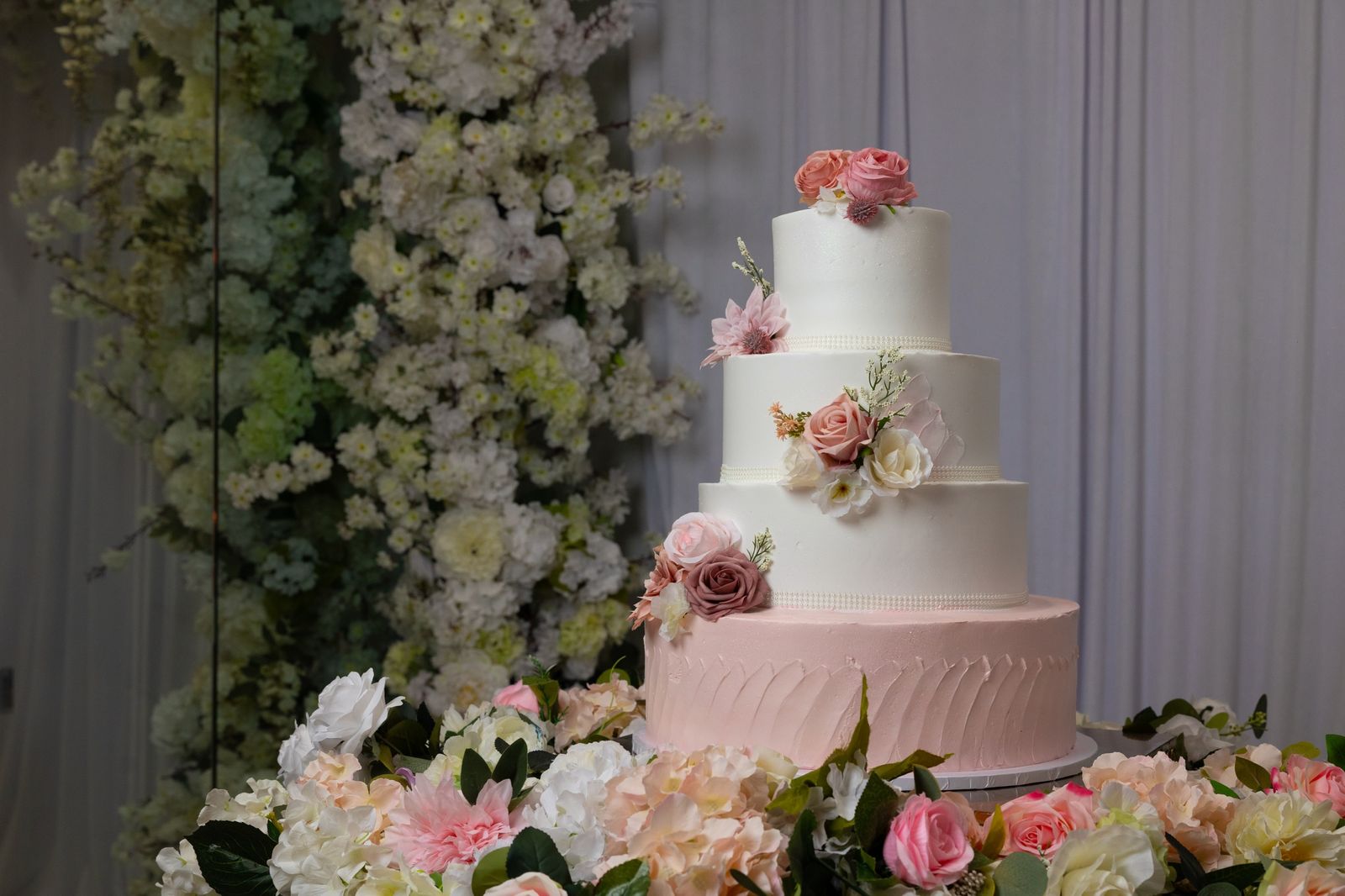 A white tiered cake surrounded by roses