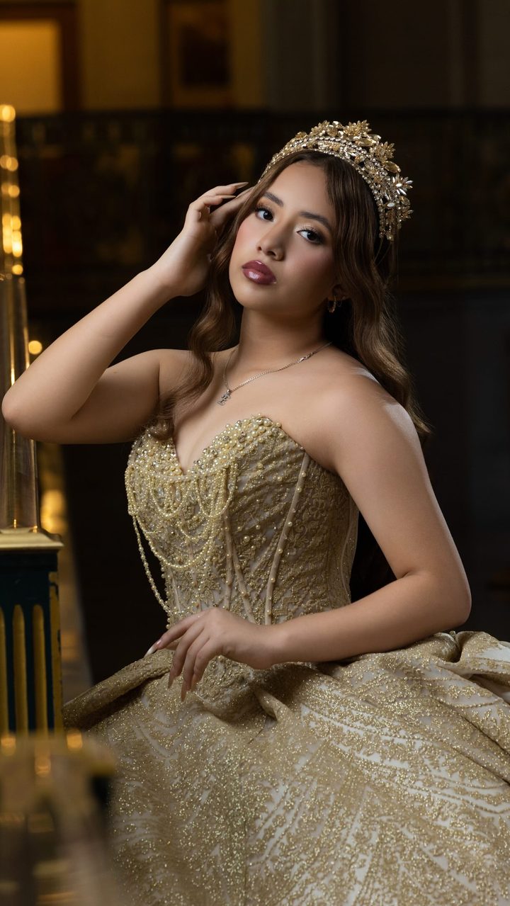 Quinceañera in a gold beaded gown and crown in an ornate hall