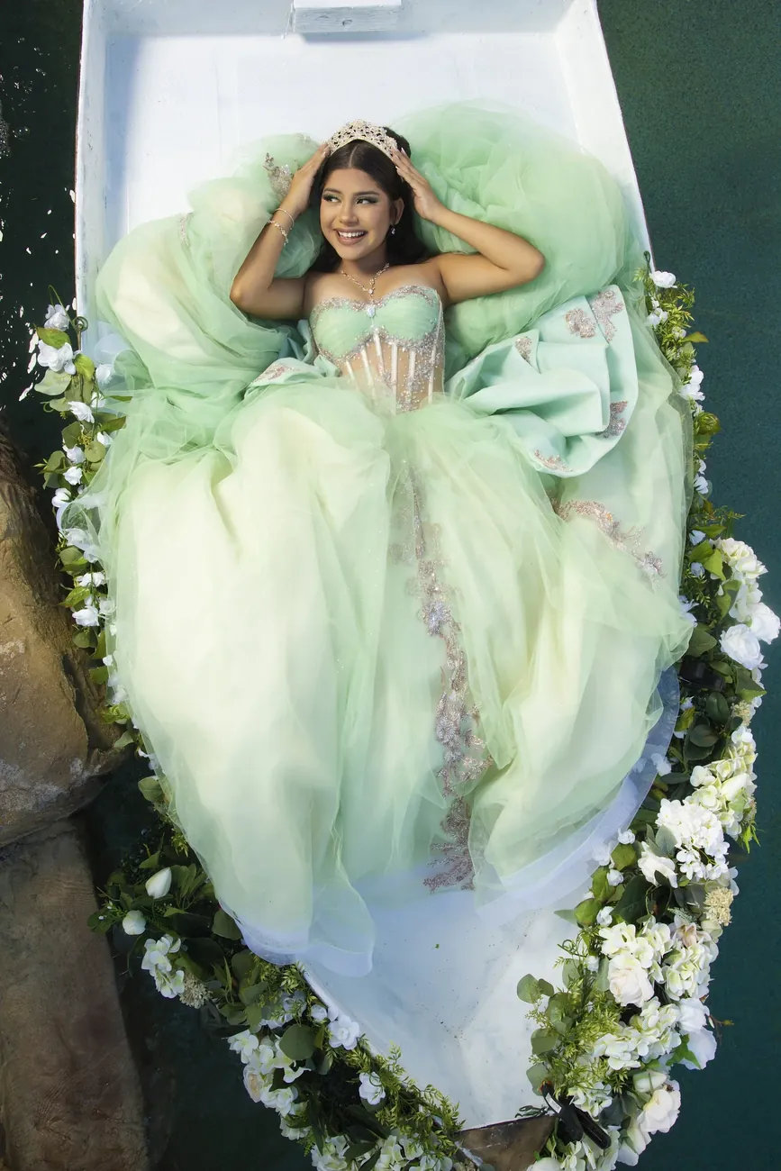 Quinceañera in a mint gown lying in a flower-lined boat